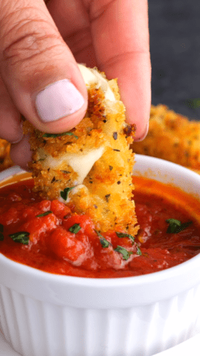 Golden mozzarella stick being dipped into bright red marinara sauce