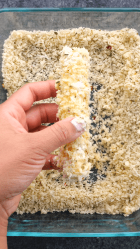 Mozzarella stick being dredged in a breadcrumb mixture