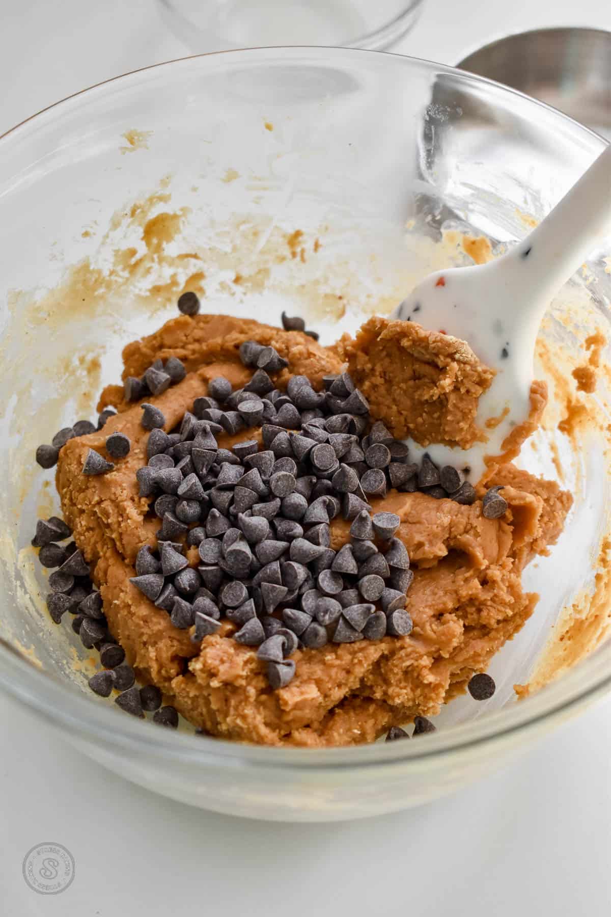 Peanut butter cookie dough covered with mini chocolate chips in a small mixing bowl