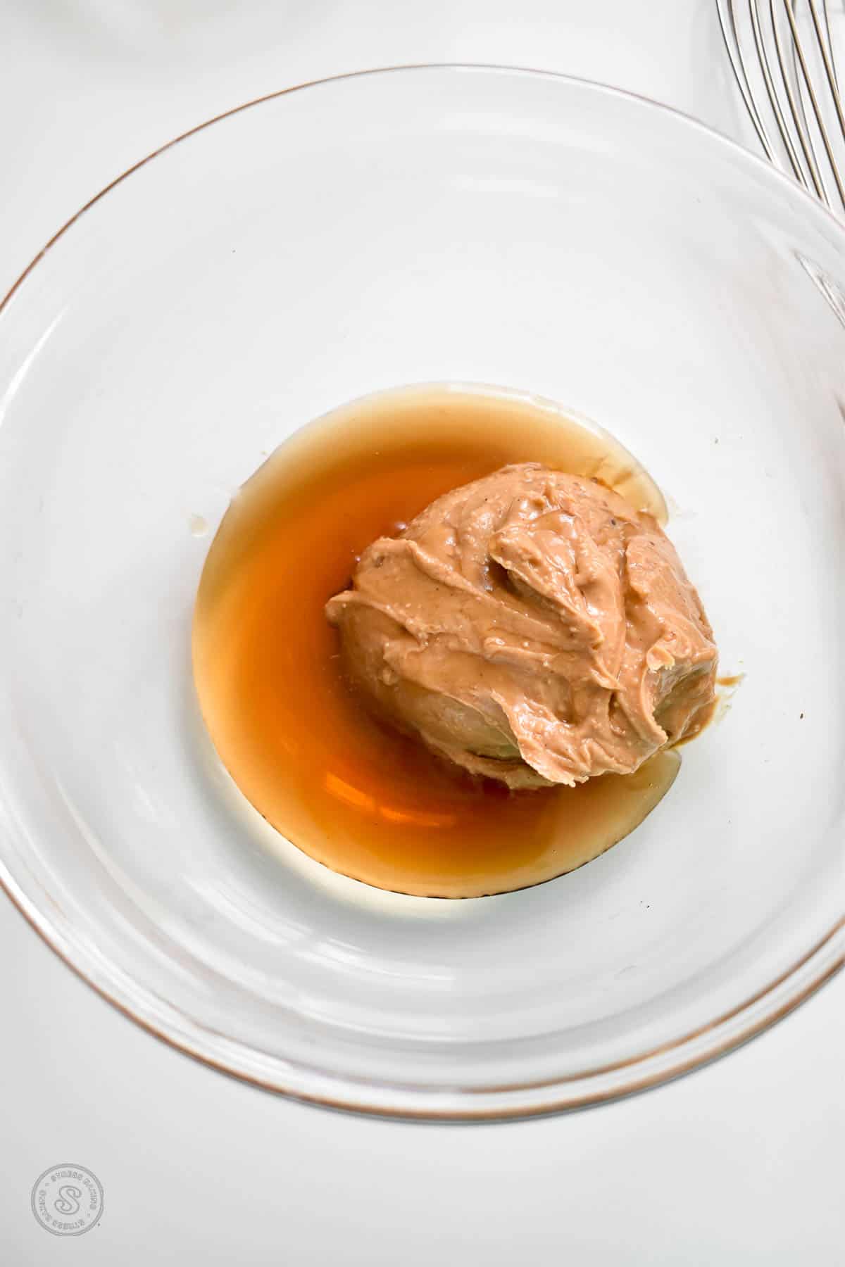 Peanut butter and maple syrup in a small clear mixing bowl