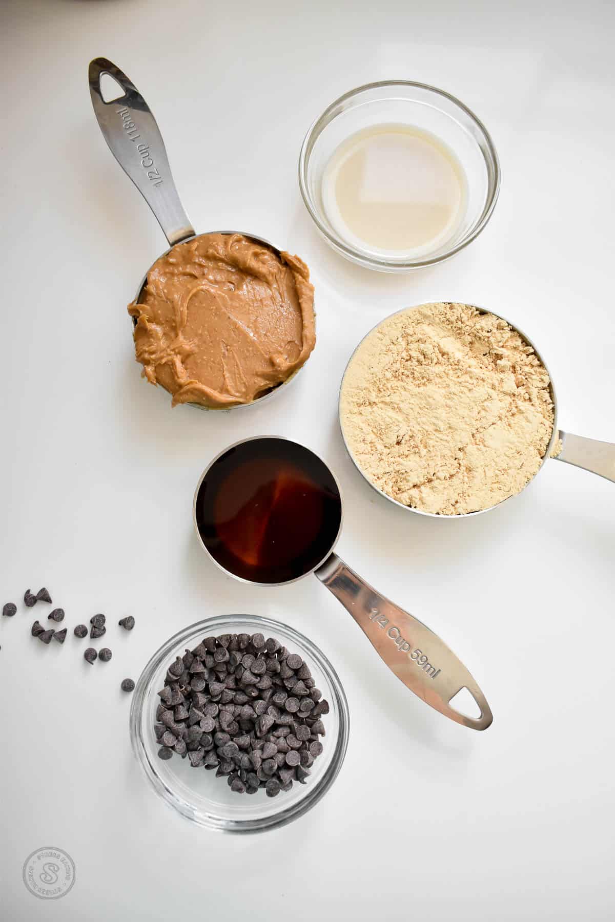 Ingredients for peanut butter cookie dough in measuring cups and clear bowls on a white countertop