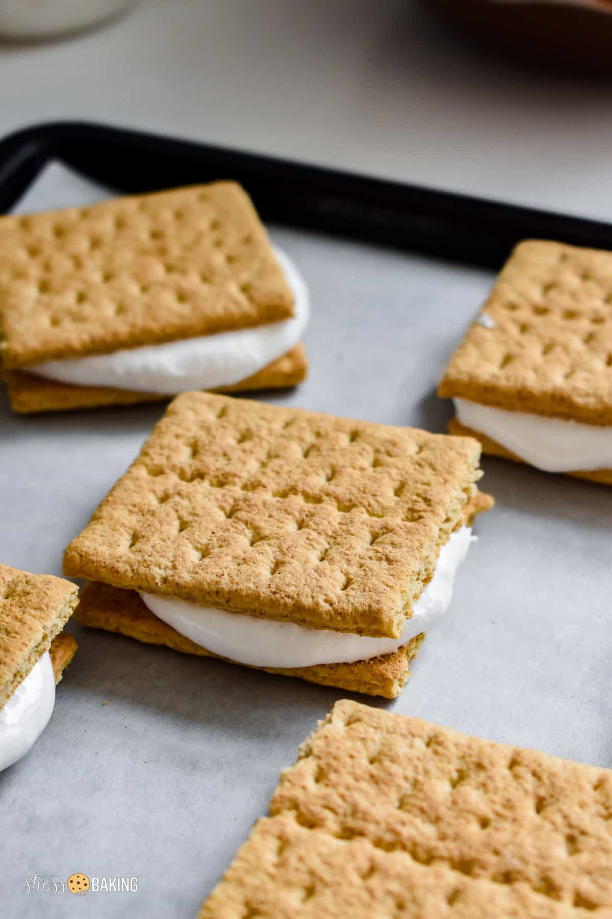 Marshmallow fluff sandwiched between two graham crackers on parchment paper on a baking sheet