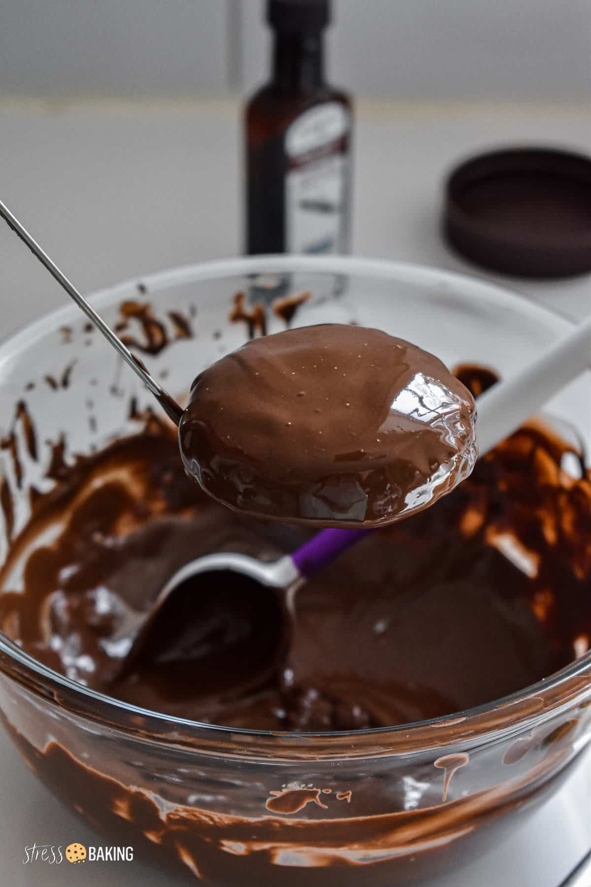 A cookie freshly coated in chocolate being held by a candy dipped above a bowl of melted chocolate