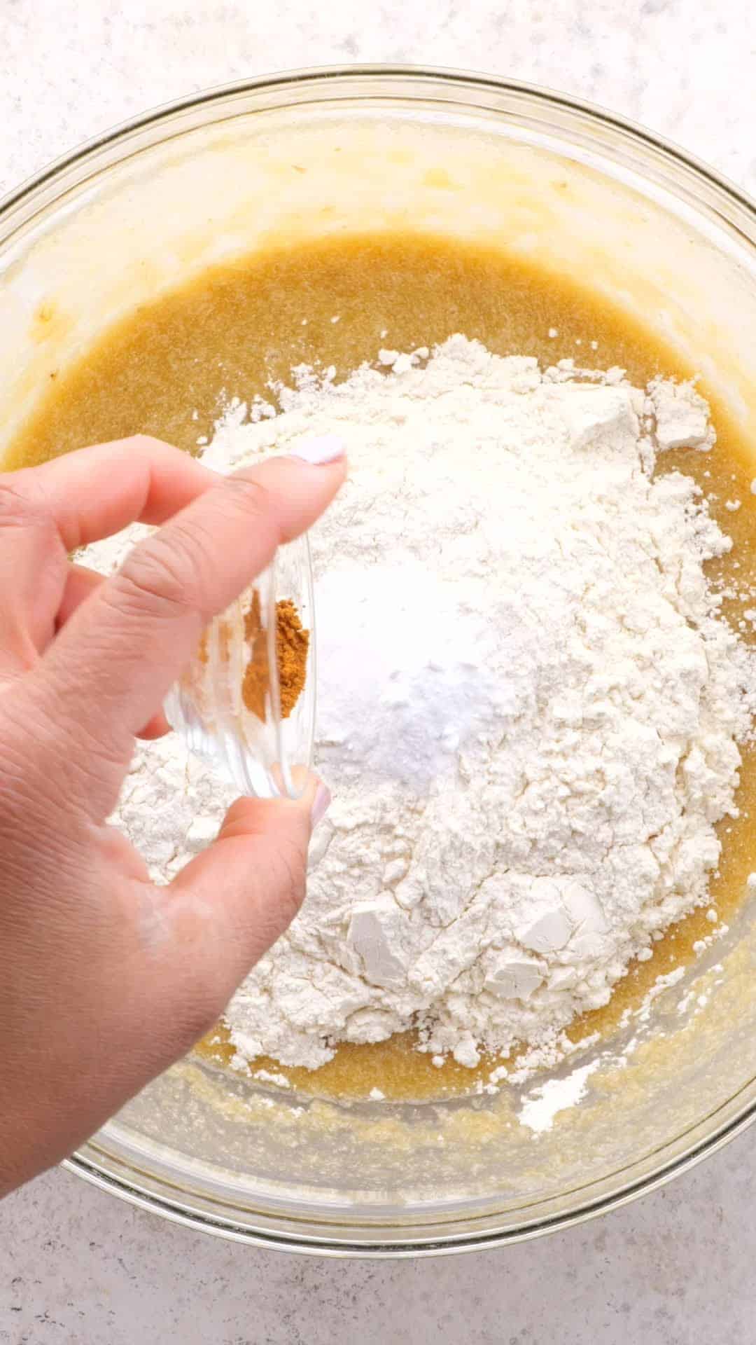 Dry ingredients being added to a bowl of tan colored batter