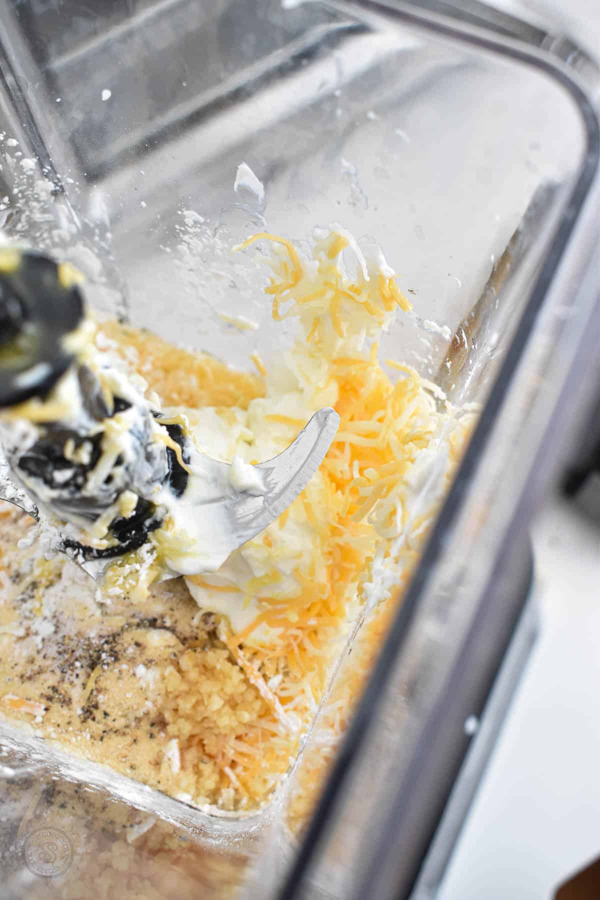 Yellow wet ingredients like yogurt and shredded cheese in a blender