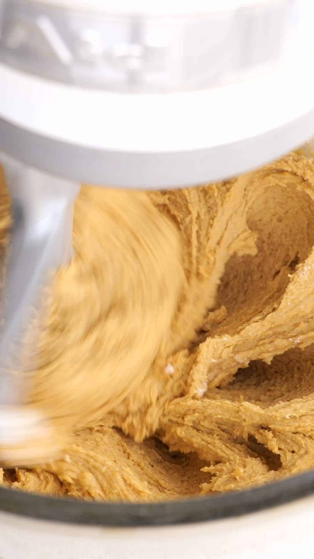 Peanut butter cookie dough being beaten in a stand mixer