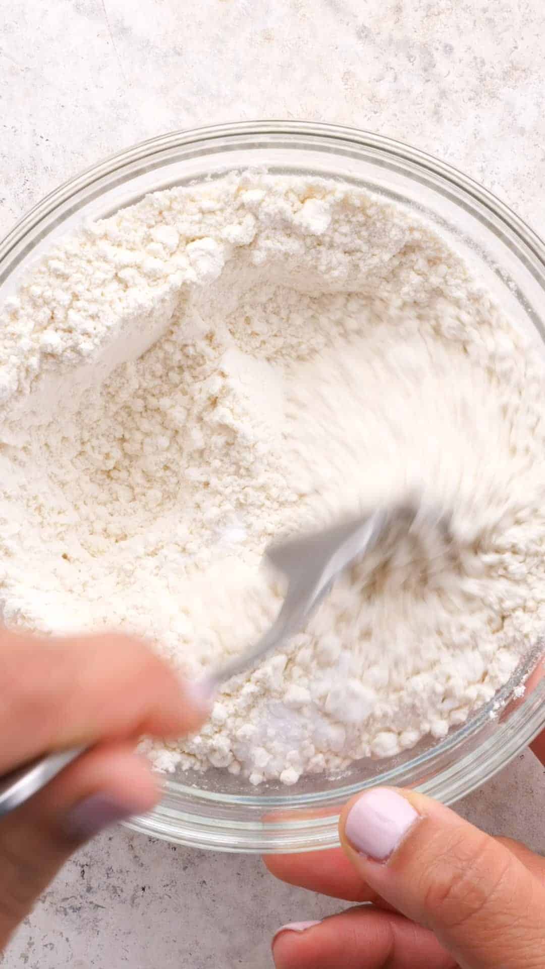 White dry ingredients being mixed with a fork in a clear bowl
