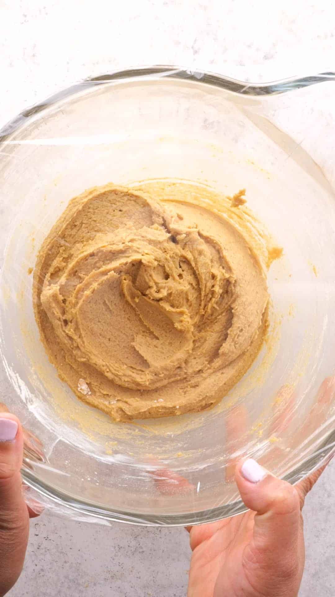Peanut butter cookie dough in a clear mixing bowl covered in plastic wrap