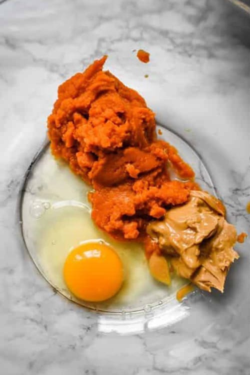 A clear mixing bowl filled with pumpkin puree, peanut butter and an egg