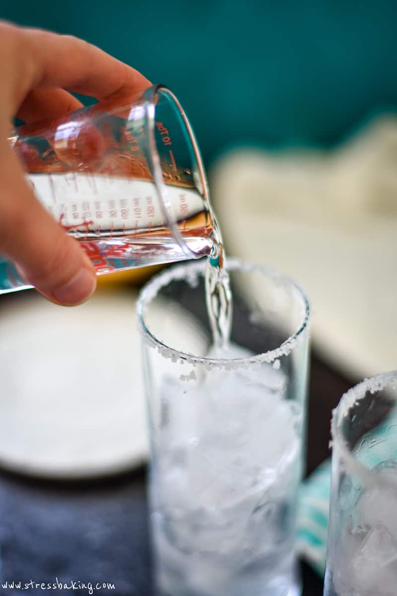 Clear alcohol being poured into a highball glass with a salted rim and filled with glass
