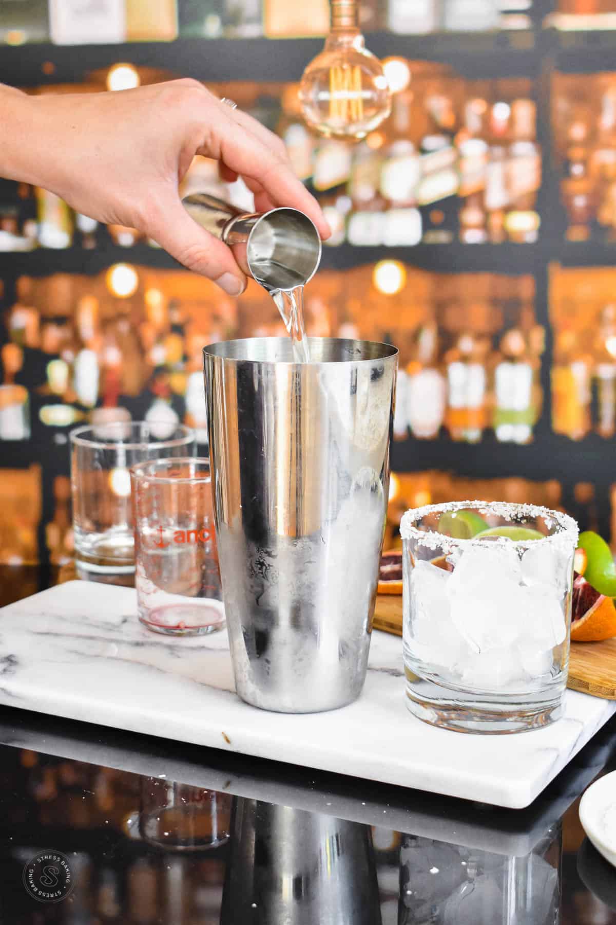 Cointreau being poured into a cocktail shaker on a white marble tray next to a salted rimmed rocks glass