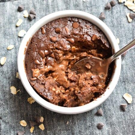 A white ramekin filled with chocolate oatmeal and a spoon digging in to show the melty chocolate center