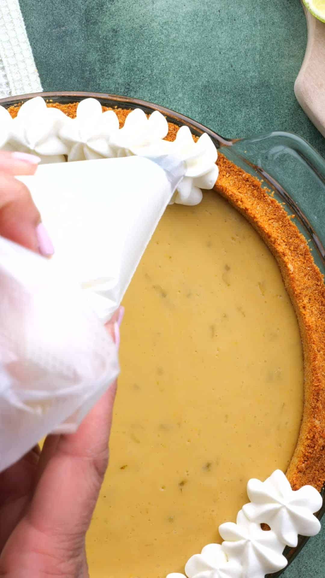 Whipped cream being piped around the crust of a key lime pie