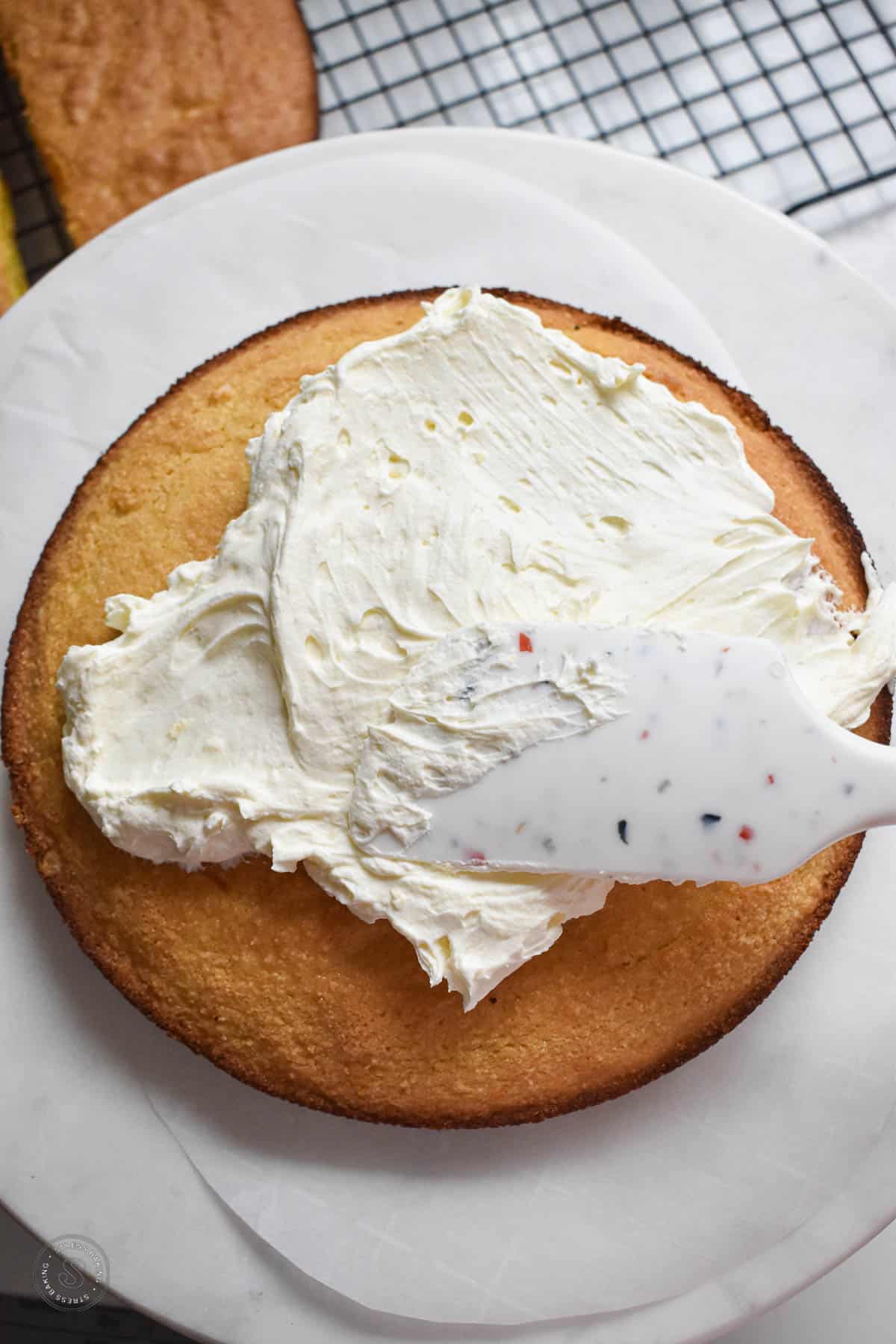 Whipped cream frosting being spread on top of a layer of yellow cake