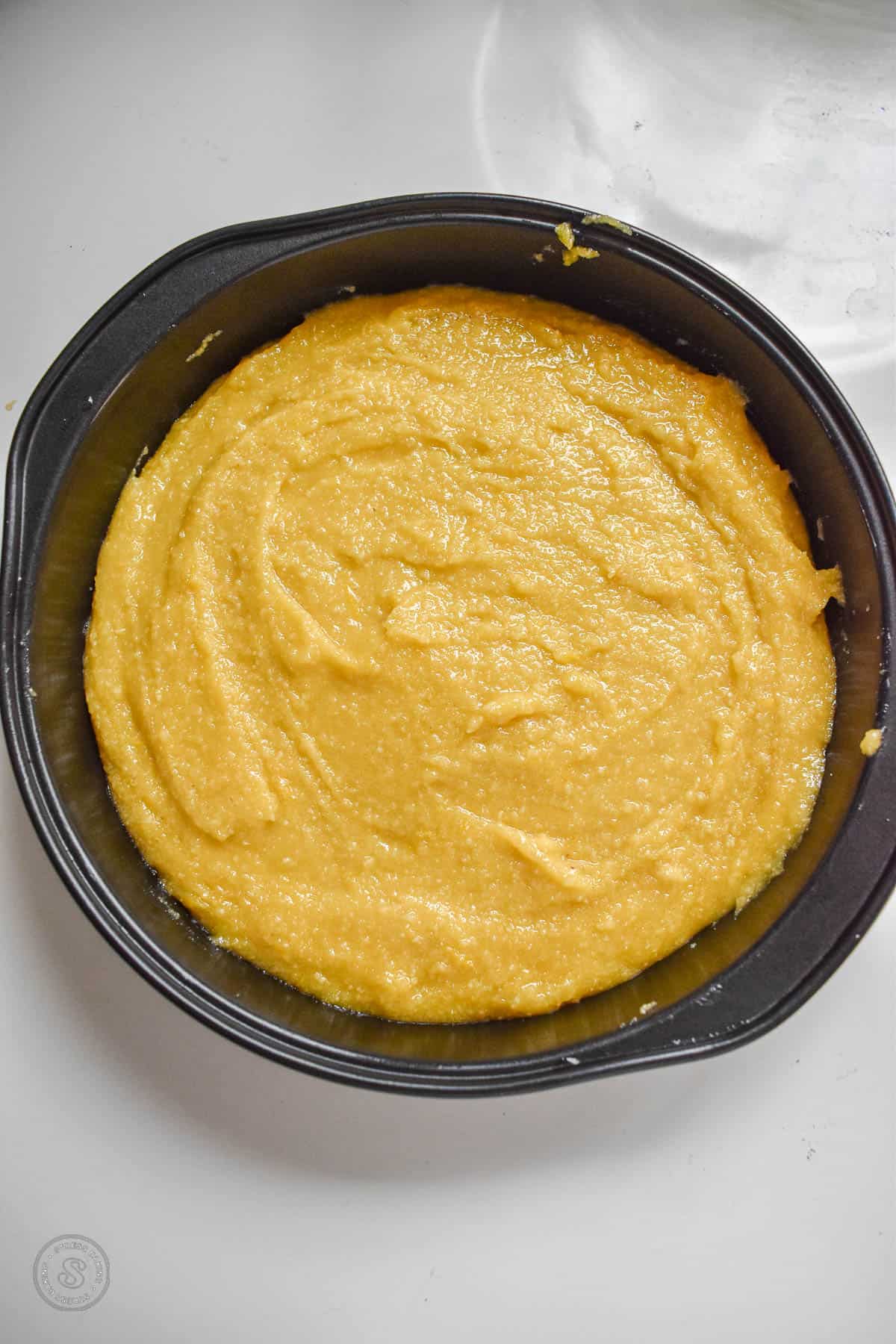 Yellow cake batter in a dark round cake pan