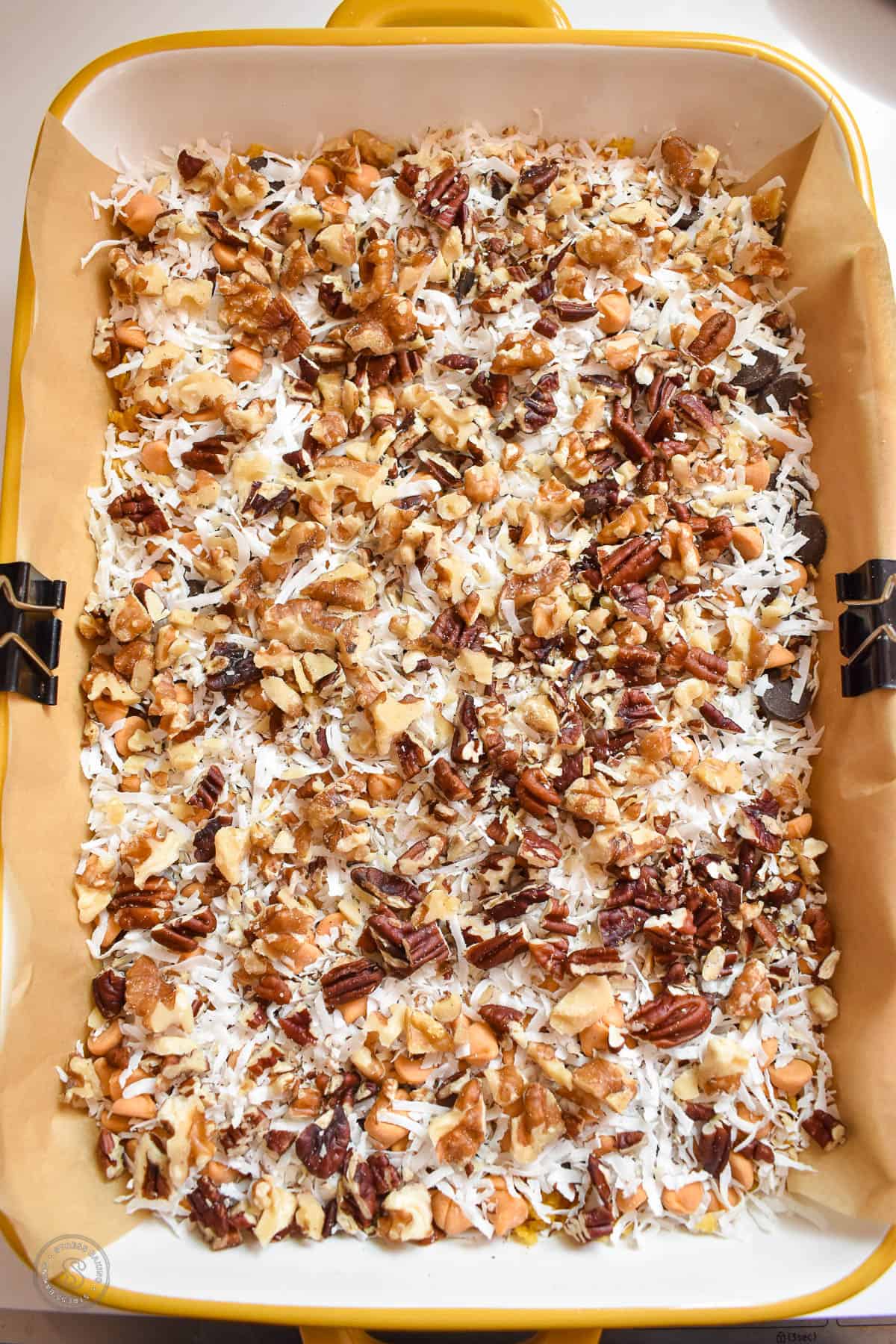 Chopped walnuts and pecans on top of shredded coconut in a baking dish
