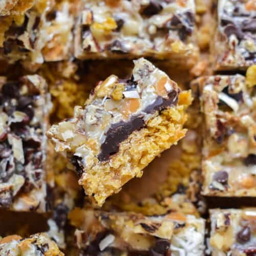 Sliced squares of magic cookie bars topped with chocolate and toasted nuts on top with one on its edge showing all the layers