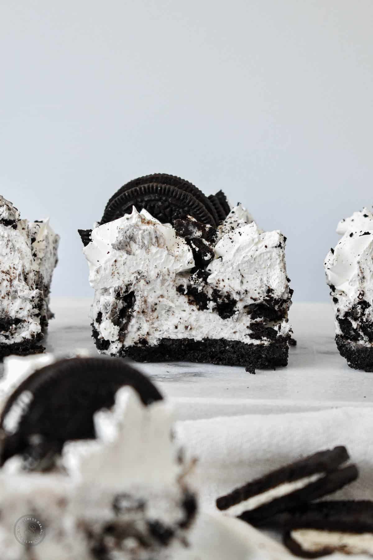 Slice of Oreo no bake dessert with an Oreo crust and black and white filling topped with whipped frosting and Oreo garnish