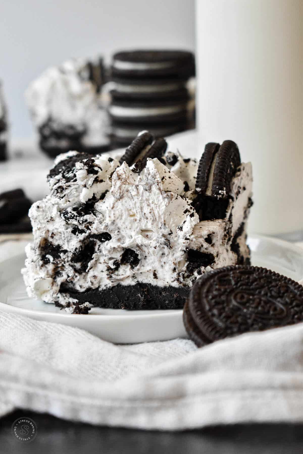 Slice of Oreo no bake dessert with an Oreo crust and black and white filling topped with whipped frosting and Oreo garnish with a glass of milk