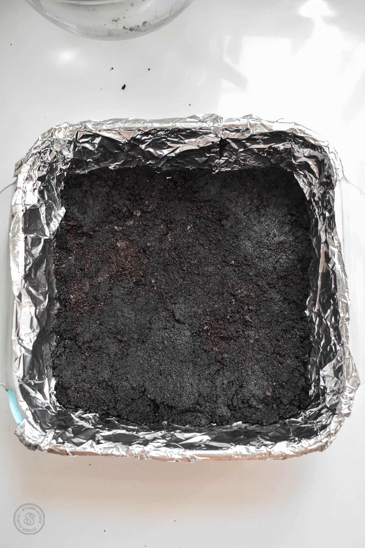 Oreo crust in a baking pan lined with foil