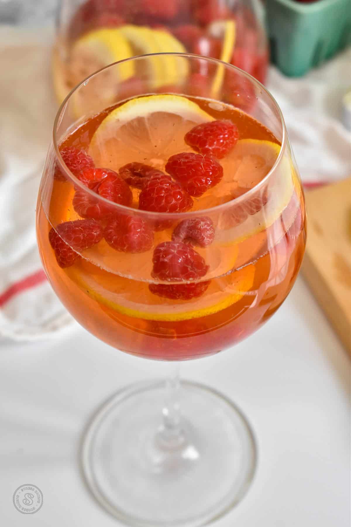 A globe wine glass filled with sliced lemons, raspberries and pink rose wine