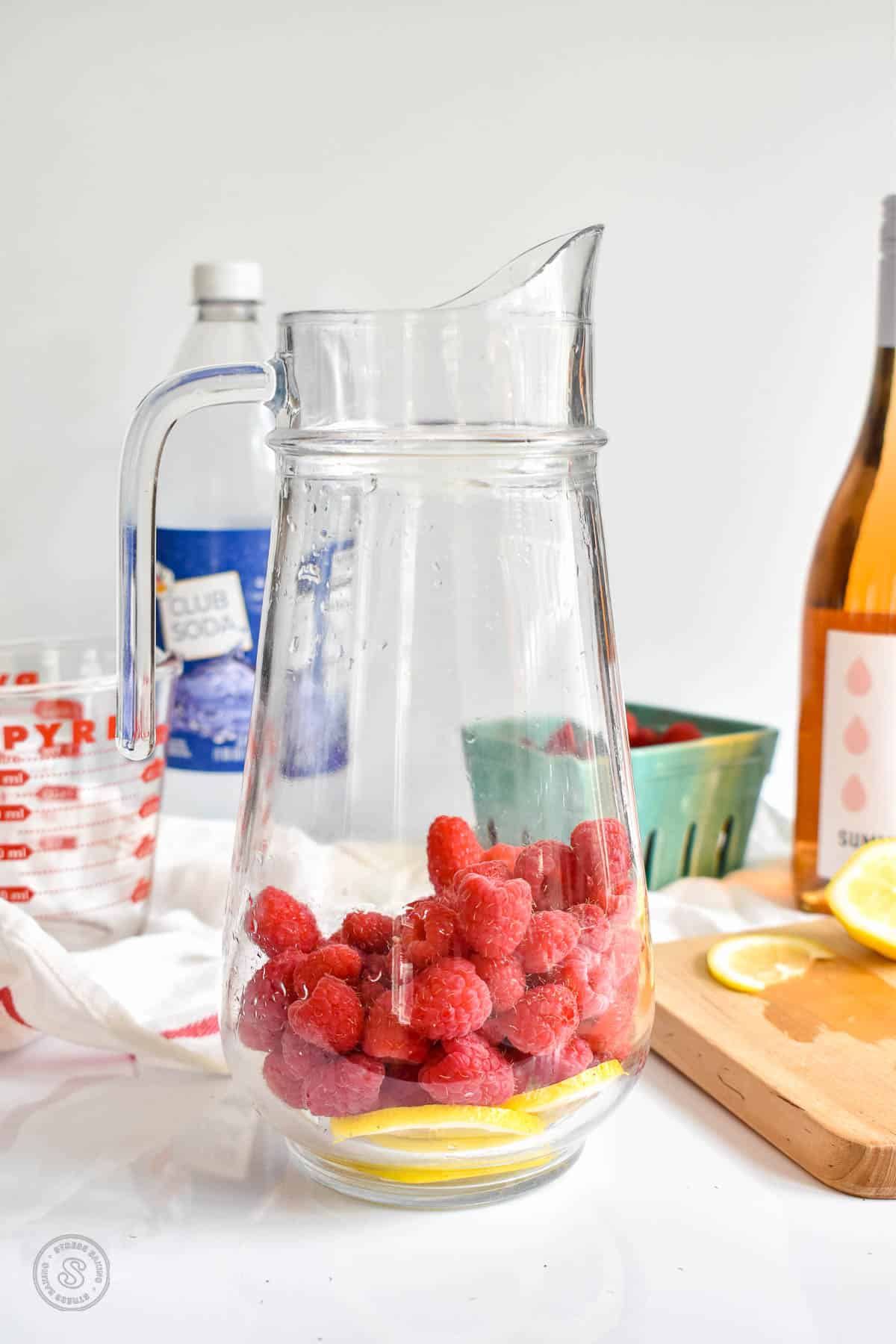 Thinly sliced lemons and raspberries in a clear pitcher