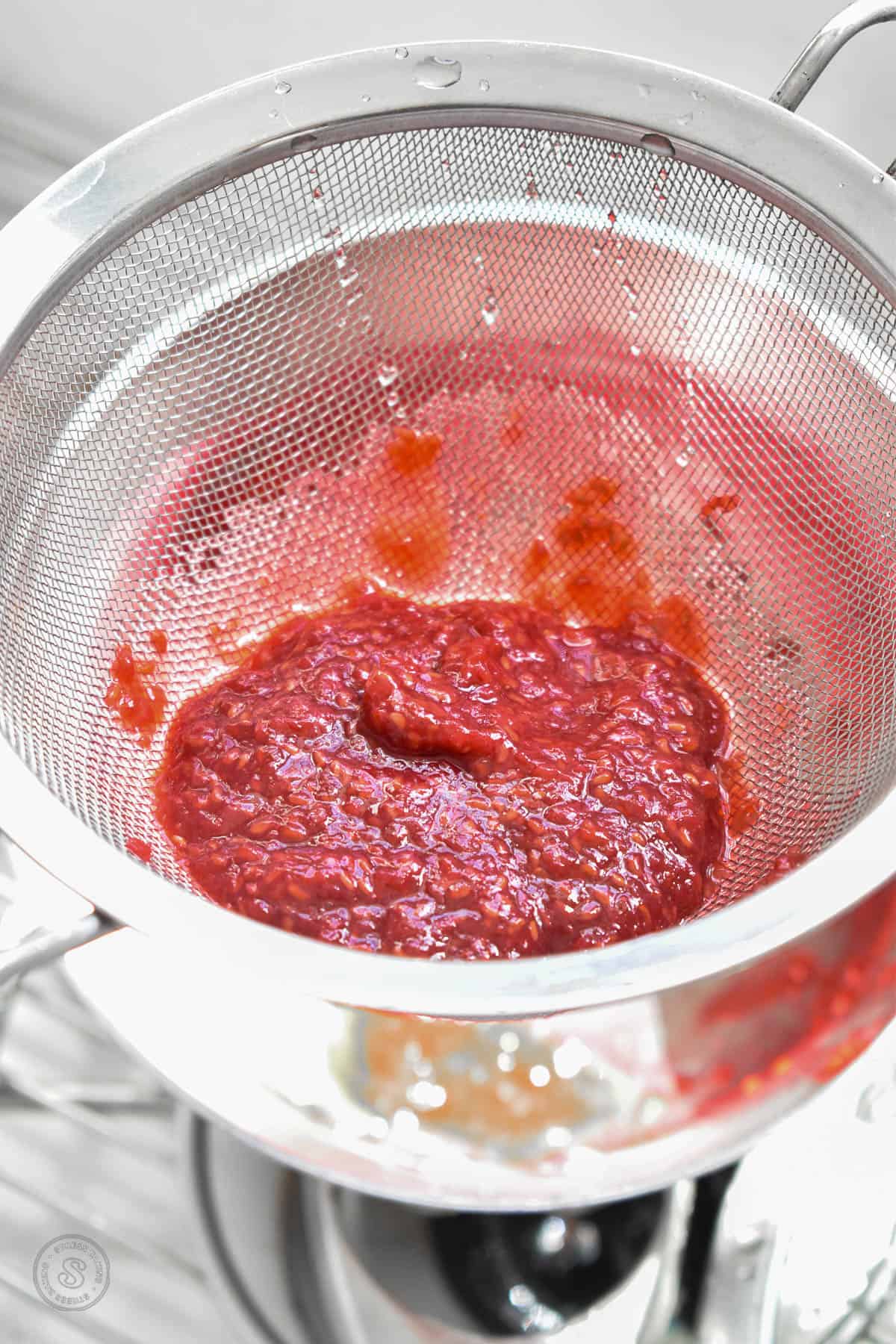 Raspberry jam being pressed through a fine mesh sieve to get the syrup