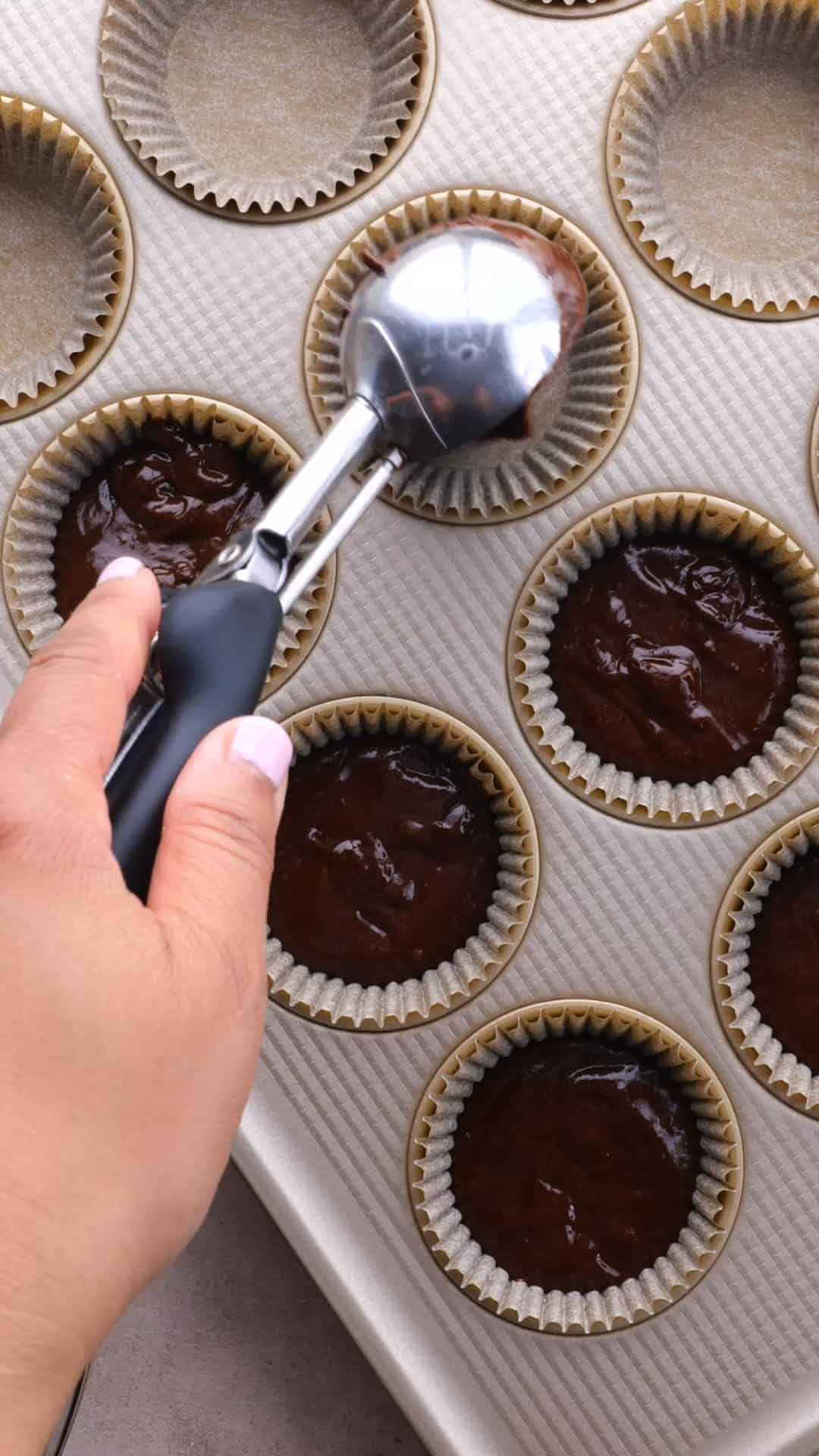 Chocolate batter being divided between cupcake liners with a large cookie scoop