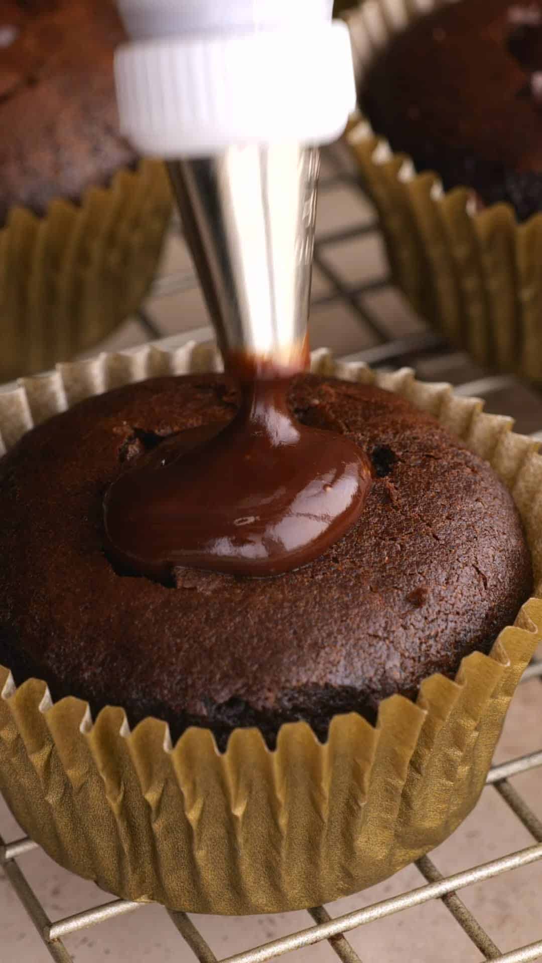 Chocolate ganache being piped into a chocolate cupcake