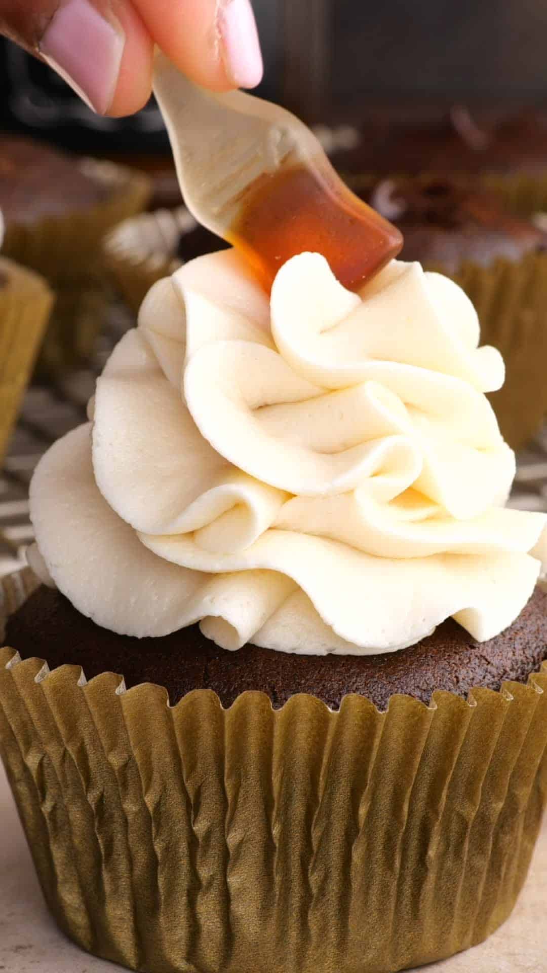 A gummy cola bottle candy being placed on top of the frosting on a chocolate cupcake