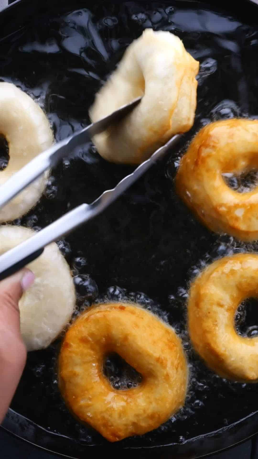 Canned biscuit dough donuts being fried in a black skillet