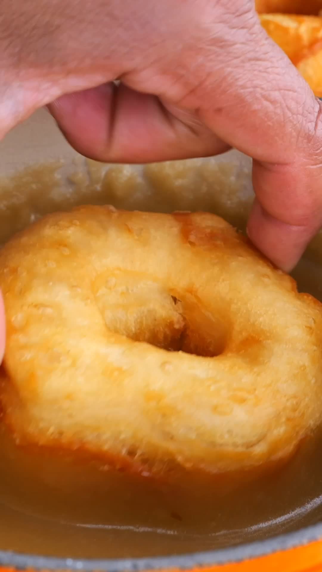 A donut being dipped in a maple glaze