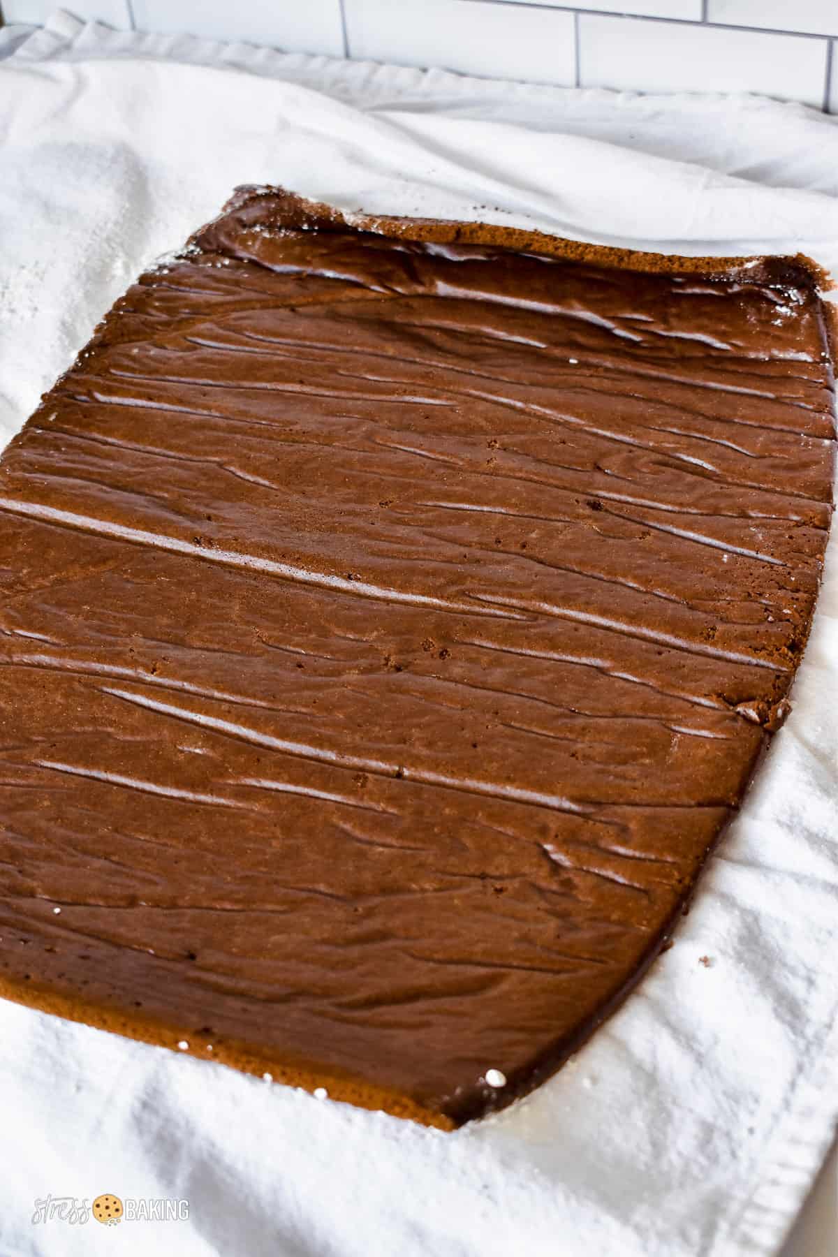 A cooled, thin layer of chocolate cake unrolled on a white kitchen towel