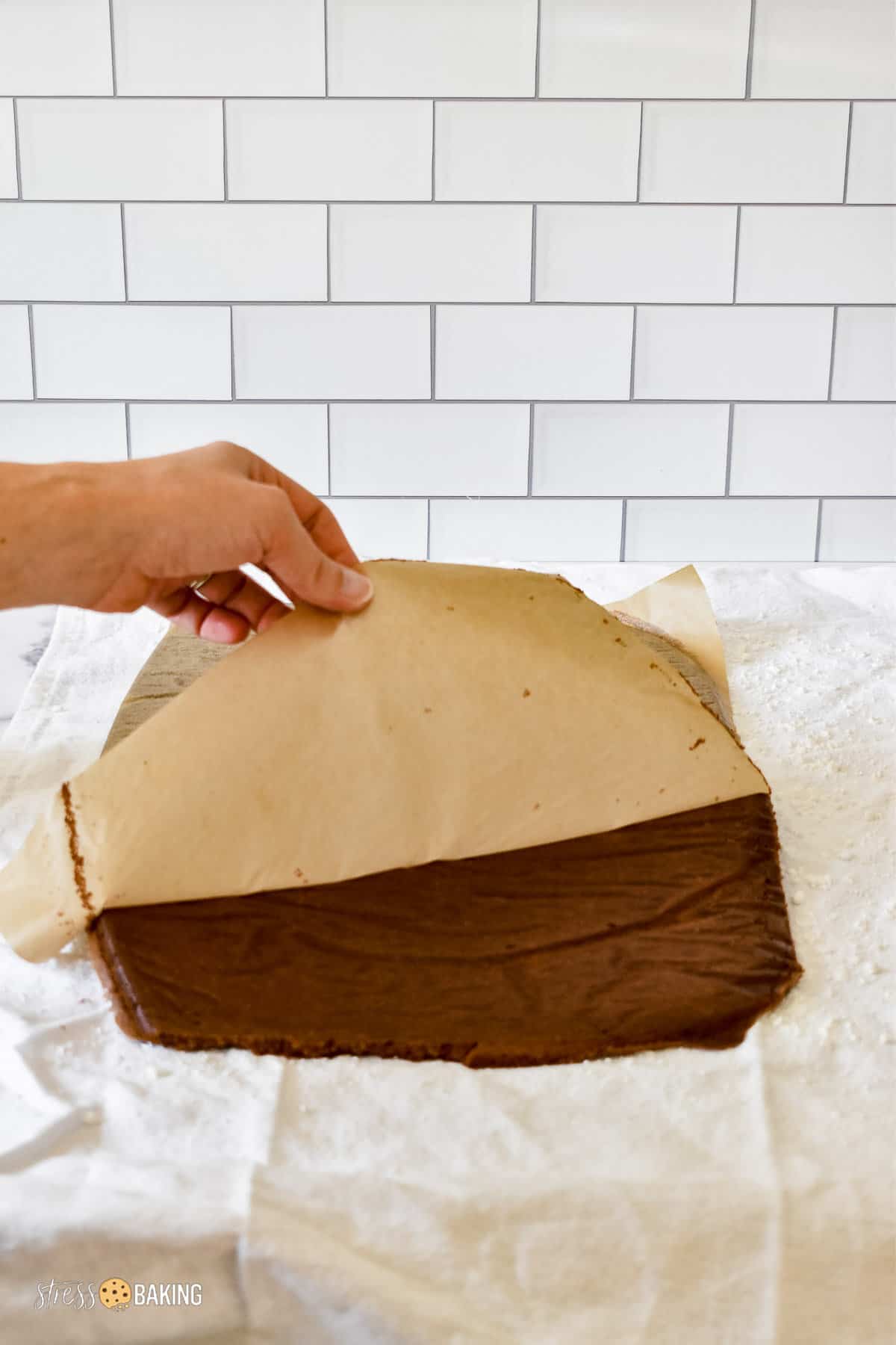 Peeling parchment paper off the back of a thin layer of baked cake on a powdered sugar coated kitchen towel
