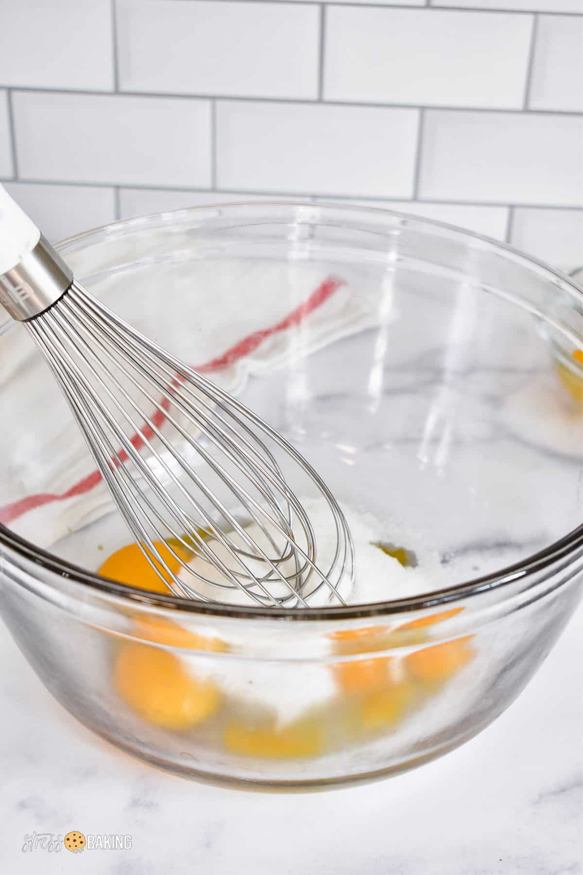 Whisking white granulated sugar and egg yolks together in a clear mixing bowl