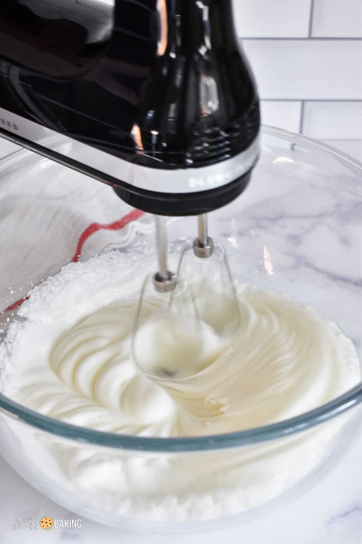 Black electric hand mixer whipping egg whites in a clear mixing bowl
