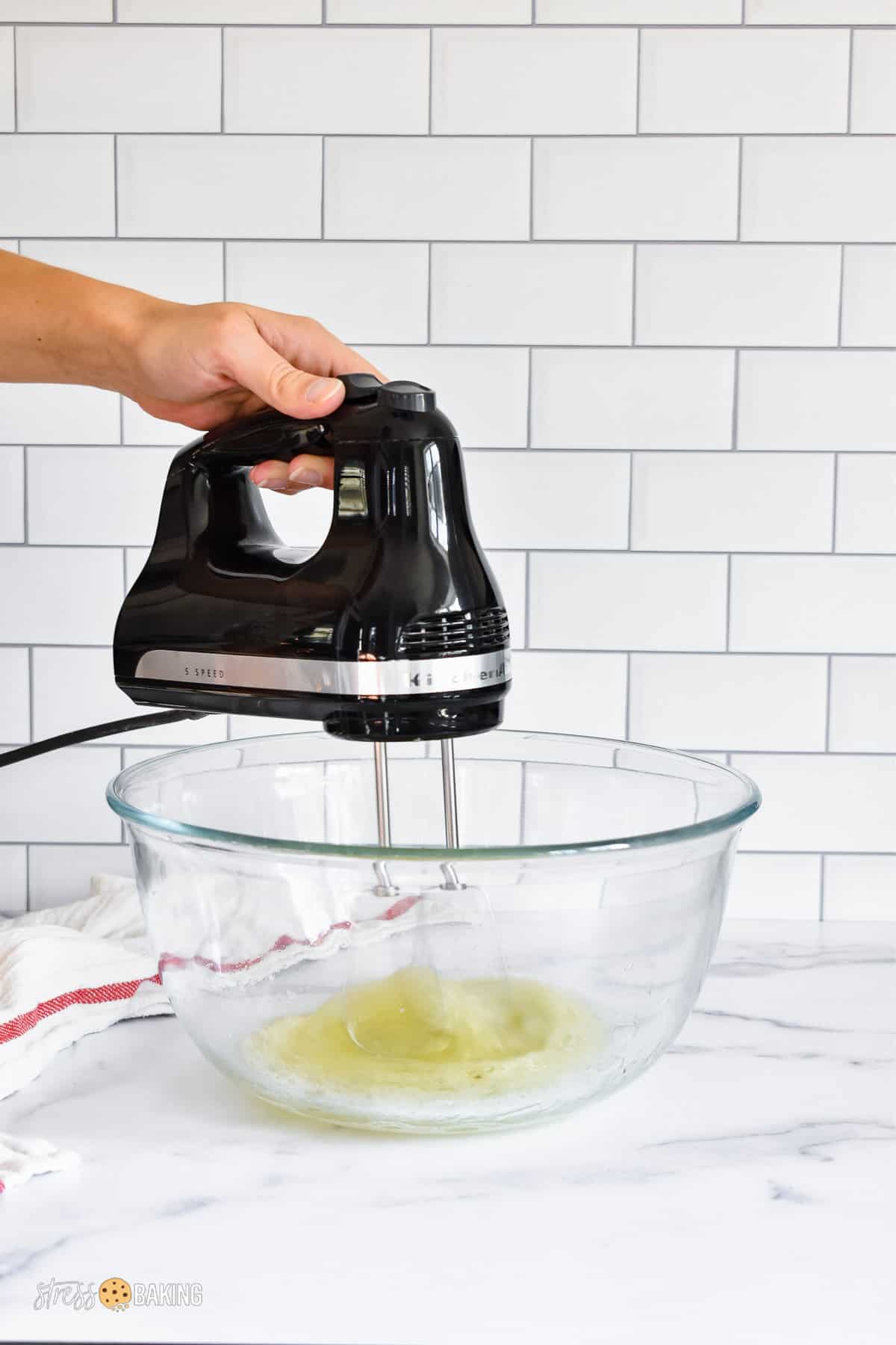 Black electric hand mixer whipping egg whites in a clear mixing bowl