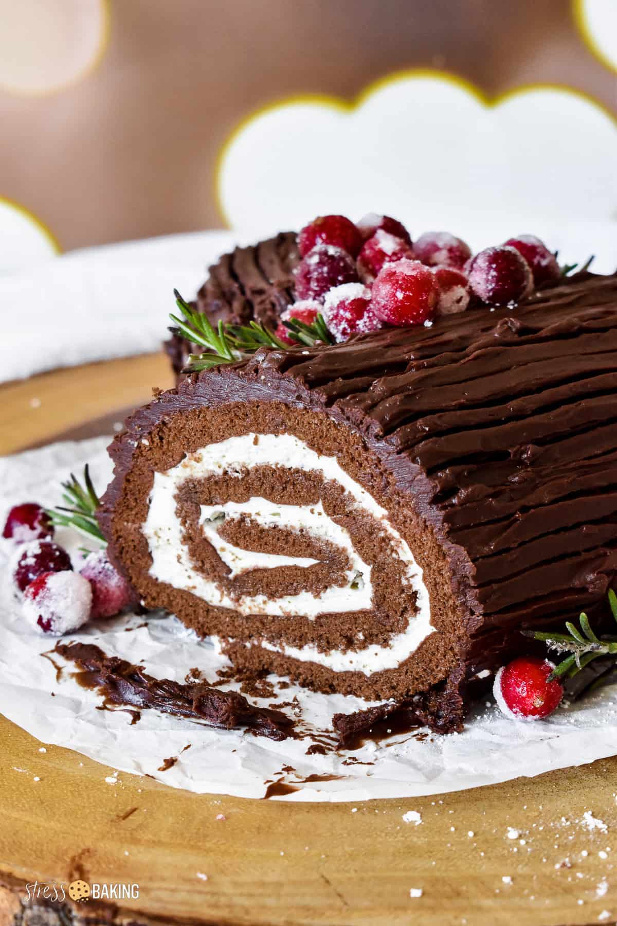 Chocolate yule log cake filled with whipped cream and decorated with sugared cranberries and rosemary twigs