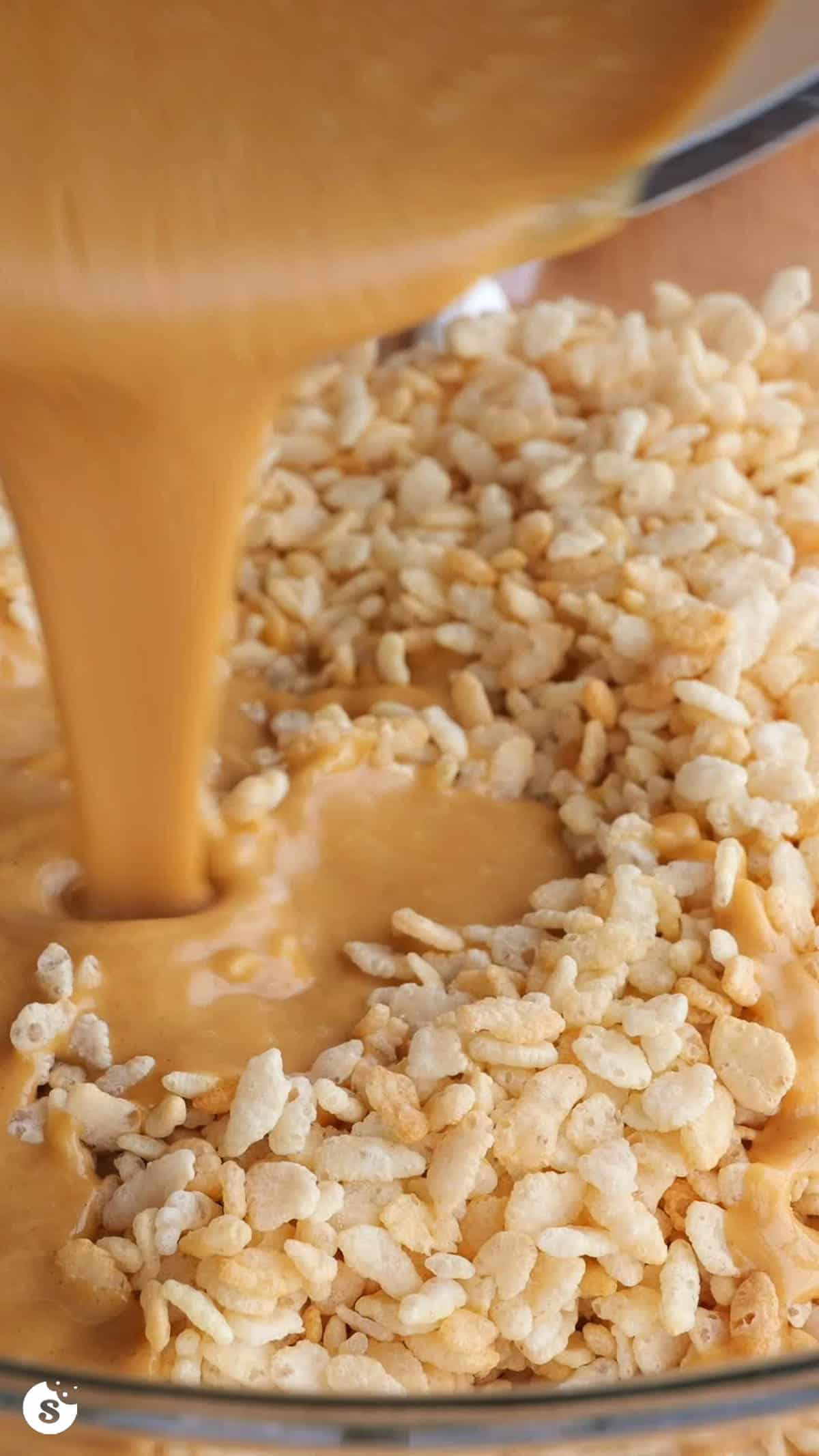 Melted peanut butter being poured into a bowl of rice krispies