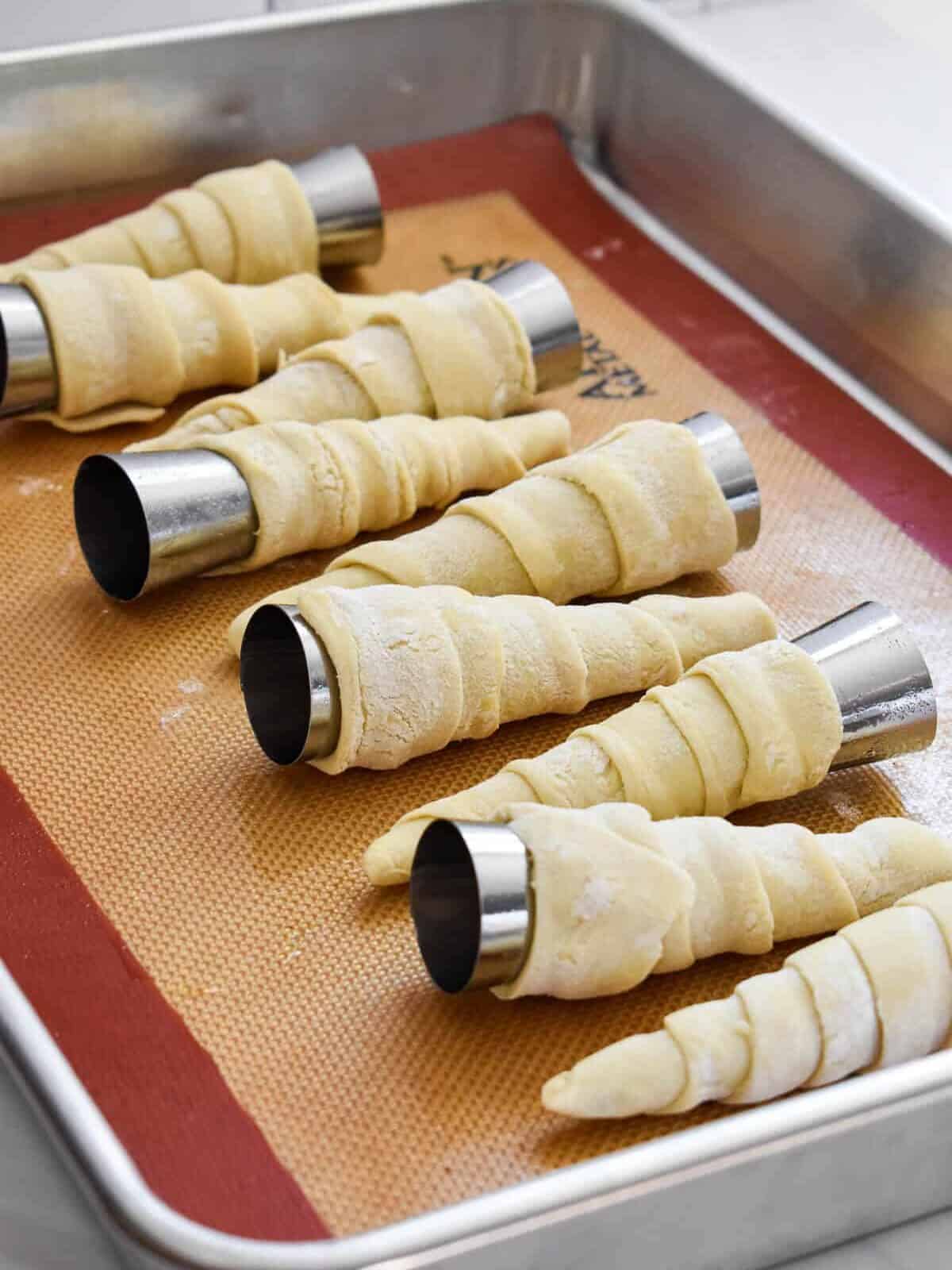 Metal pastry cones wrapped with puff pastry strips on a baking sheet