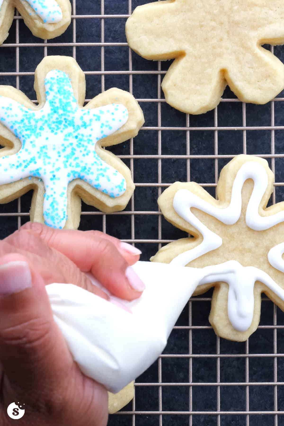White icing being piped onto snowflake sugar cookies