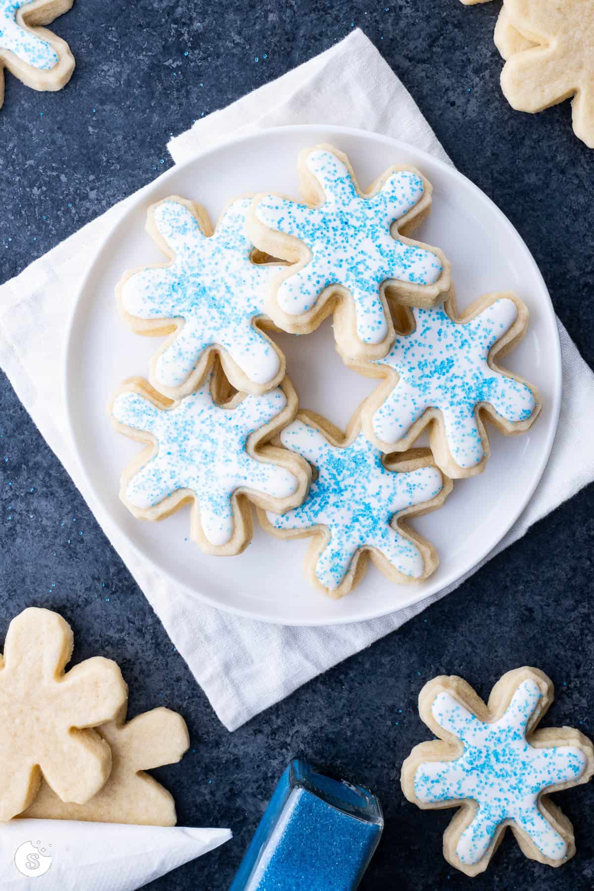 Snowflake sugar cookies on a white plate decorated with white icing and blue sprinkles